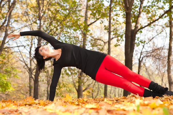 Pretty woman doing yoga exercises in the autumn park - Fotoğraf, Görsel