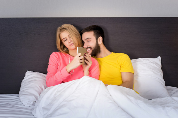 Молодая сладкая пара в постели Смотря что-то на планшетном гаджете
 - Фото, изображение