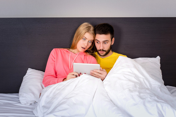 Giovane dolce coppia a letto guardando qualcosa su tablet gadget
 - Foto, immagini