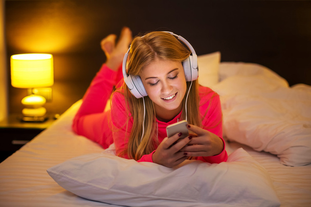 Νεαρές γυναίκες που ακούτε τη μουσική από το smartphone στο κρεβάτι - Φωτογραφία, εικόνα