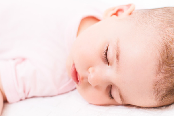 白いベッドの上に寝ている女の赤ちゃんの愛らしい、美しいクローズ アップ肖像画. - 写真・画像