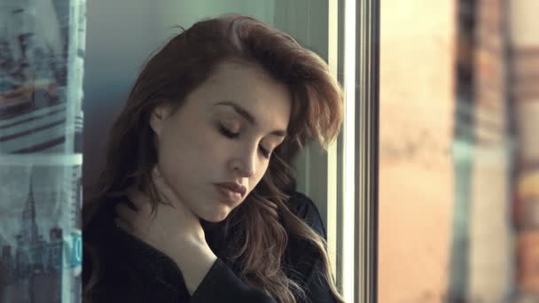 mujer pensativa y problemática masajea su cuello cerca de la ventana
 - Metraje, vídeo