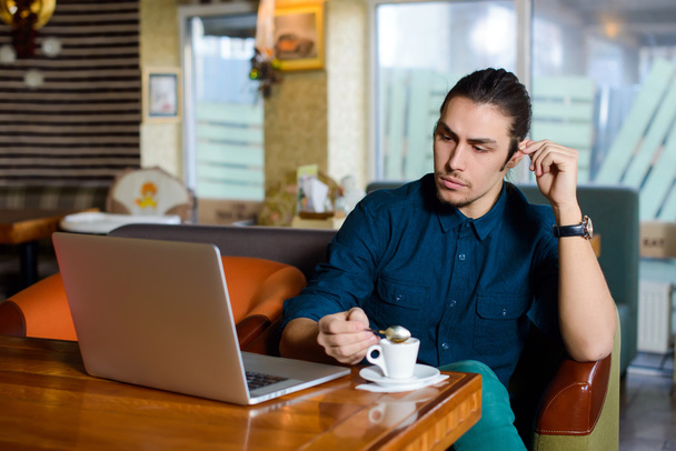 Young man drinking coffee and working on laptop in a cafe - Фото, изображение