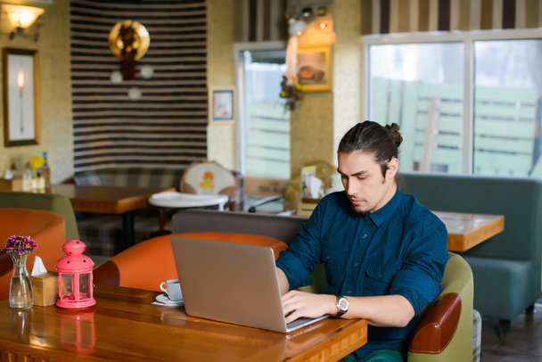 Молодий чоловік п'є каву і працює на ноутбуці в кафе
 - Фото, зображення