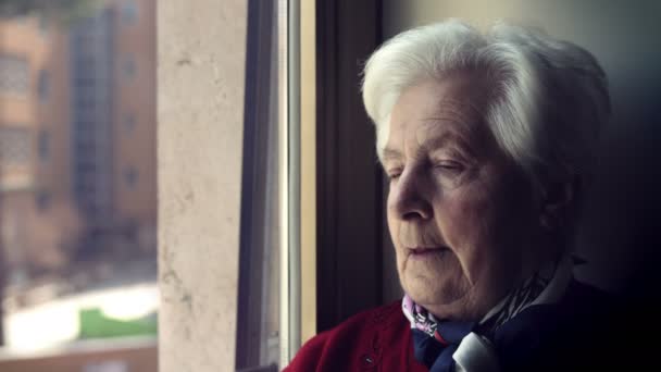 sad old woman looking out the window: elderly depressed woman portrait - Záběry, video