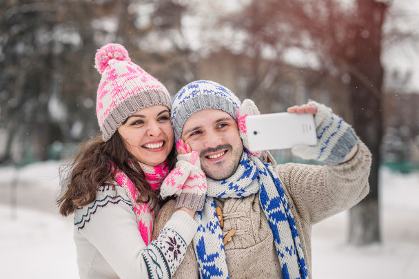 пара закохана посміхається і робить селфі взимку на відкритому повітрі
 - Фото, зображення