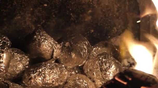 Aardappelen verpakt in folie bakken in de sintels in de open haard. - Video