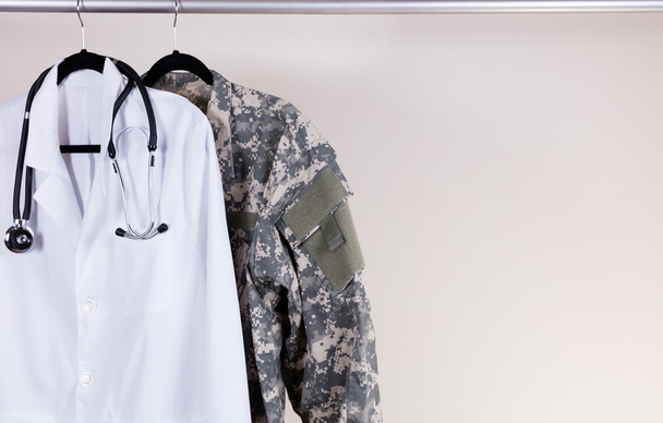 Weißer Arztkittel und Militäruniform am Kleiderbügel  - Foto, Bild