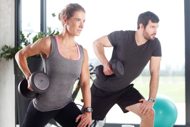 Woman and man lifting barbells at fitness center - Foto, immagini