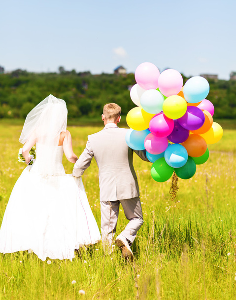 Braut und Bräutigam auf einer Wiese mit bunten Luftballons - Foto, Bild