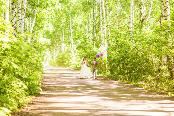 Beautiful bride holding bunch of balloons in the park. Couple of bride and groom with balloons. Newlyweds with balloons outdoors - Foto, immagini