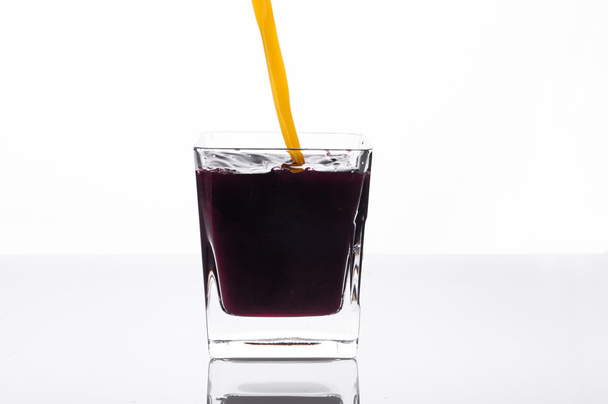 Orange juice pouring into glass with blackcurrant juice - Foto, afbeelding