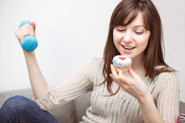 Woman exercising on sofa with cupcake in hand - Фото, изображение