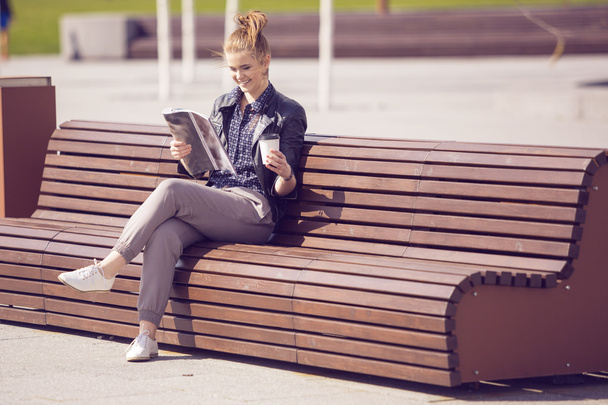 Femme souriante assise sur un banc avec café et lecture de magazin
 - Photo, image