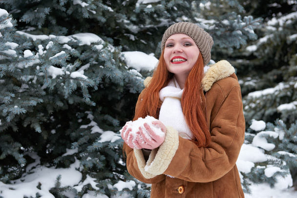 Femme prendre une poignée de neige dans le parc d'hiver le jour. Sapins avec neige
.  - Photo, image