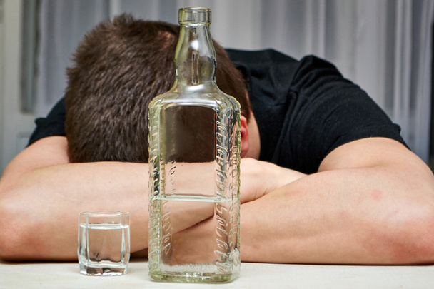 Le gars qui dort à table avec une bouteille et un verre de vodka
 - Photo, image