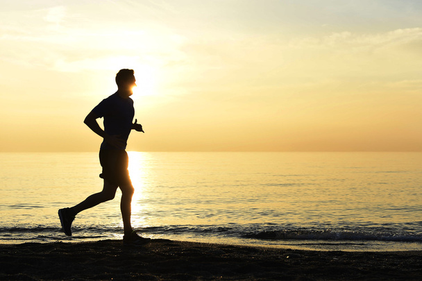 Silhouette giovane uomo sportivo correre all'aperto sulla spiaggia al tramonto con cielo arancione - Foto, immagini