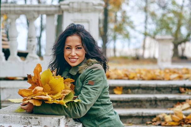 Smiling young attractive woman with autumn maple leaves in park at fall outdoors - Photo, Image