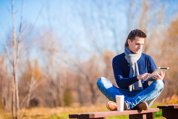 秋の公園で電話でコーヒーを飲む若い男屋外 - 写真・画像
