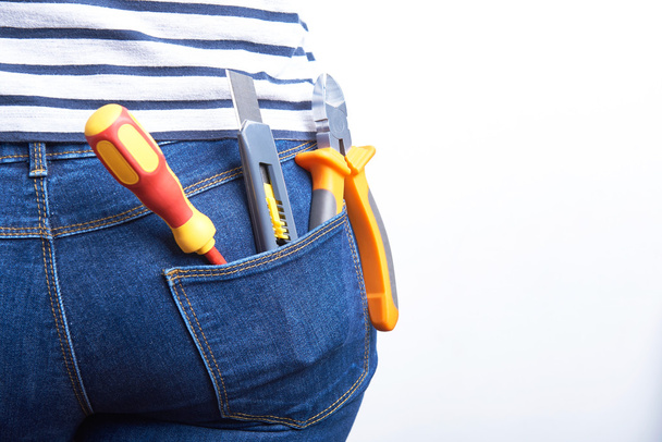 Tools for electrician in back pocket of blue jeans worn by a woman. Screwdriver, sharp knife and cutters. - Foto, afbeelding