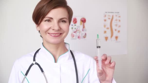 female doctor in lab coat with a stethoscope shows a syringe - Кадри, відео