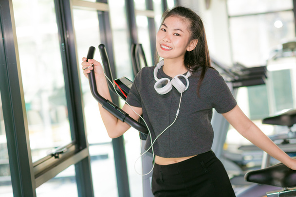Азиатка тренируется в тренажерном зале на кросс-тренере, женщина тренируется в фитнес-клубе
 - Фото, изображение