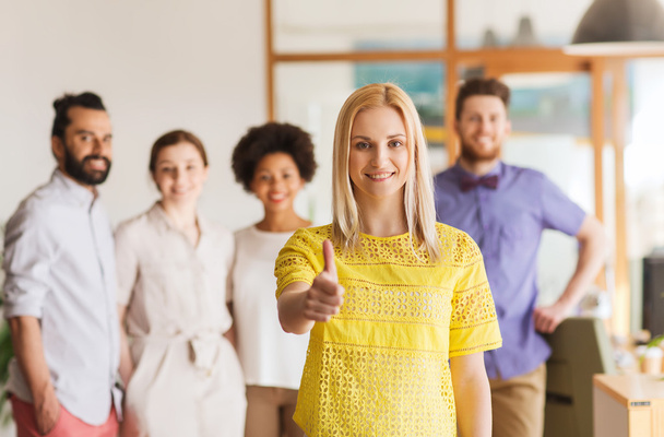 woman showing thumbs up over creative office team - Photo, Image