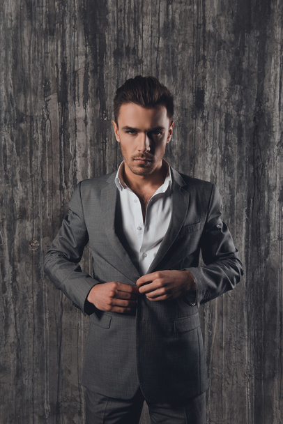 Handome man in suit on the grey background fastening buttons - Φωτογραφία, εικόνα