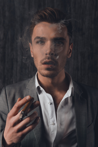 Handome sexy man in suit on the grey background smoking a cigar - Fotó, kép