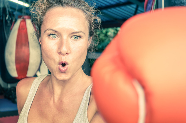 Woman hitting with punch on gritty determination - Fitness boxe and mixed martial arts concept - Fit girl on self defense technique in grungy combat center - Vintage filtered look - Sport gym is setup - Photo, Image