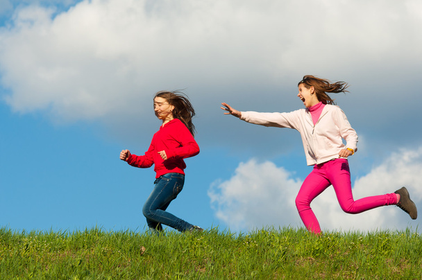 Two happy teenage girls running on the meadow on sunny spring day - Photo, Image