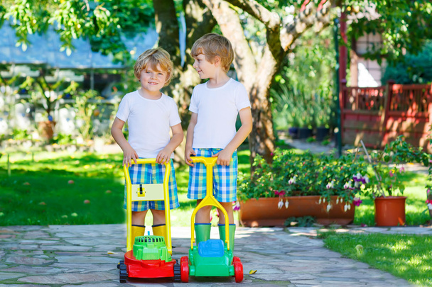 Dois meninos brincando com brinquedos de cortador de grama
 - Foto, Imagem