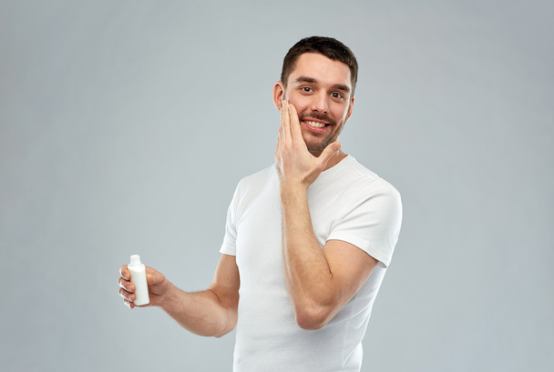 happy young man applying cream or lotion to face - Фото, зображення