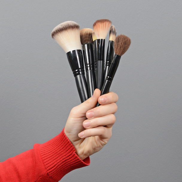 Woman hand holding make-up brushes against gray background - Фото, зображення