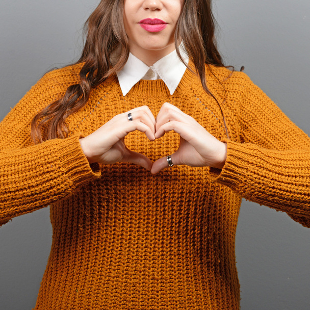 Woman forming heart shape against gray background - Fotó, kép