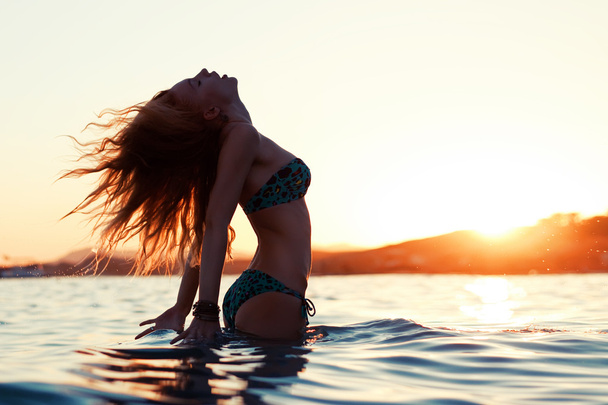 the beautiful sexy girl with long hair costs in the sea against the sunset sun - Фото, изображение