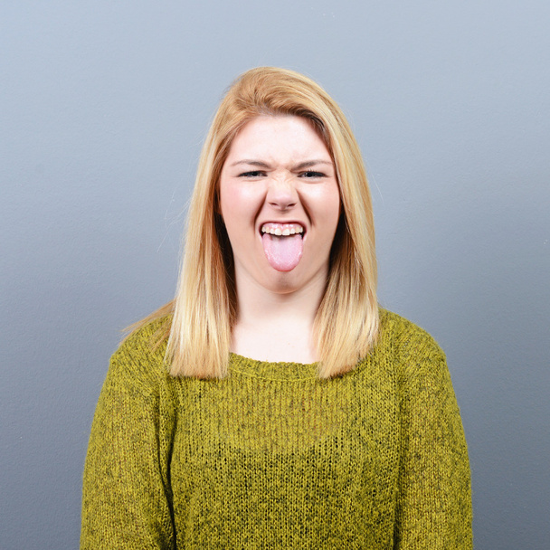 Портрет женщины, торчащей языком против серой спинки
 - Фото, изображение