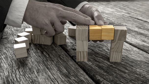 Крупним планом бізнесмен утворює міст з маленьких дерев'яних блоків
 - Фото, зображення
