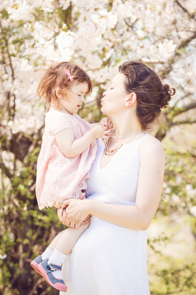 Zwangere vrouw met dochter in park knuffelen, zoenen - Foto, afbeelding