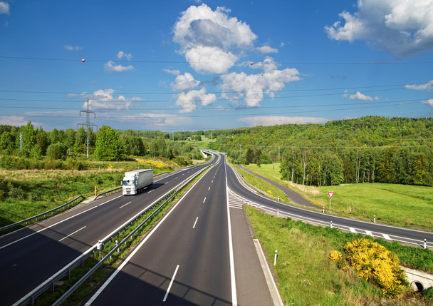 Zufahrtsstraße zur asphaltierten Autobahn zwischen Wäldern. weißer LKW unterwegs. - Foto, Bild