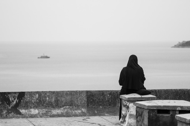 A woman in a headscarf sitting on the sea background - 写真・画像