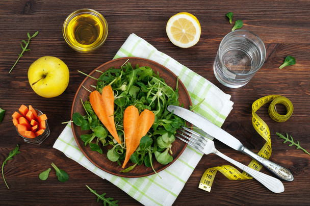 Concept diet food. Salad with arugula, leaf mash and carrots on a dark wooden background. Vegetarian healthy dish that promotes weight loss. - Photo, Image