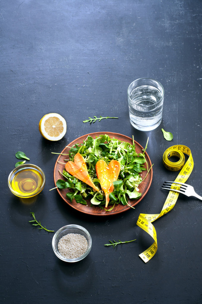 Concept diet food. Salad with arugula, leaf mash and carrots on a dark background. Vegetarian healthy dish that promotes weight loss. - Photo, Image