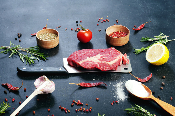Raw beef steak, which lies on the cutting knife. Raw beef meat prepared for cooking steaks. Beside the ingredients for cooking steaks, spices and herbs. - Fotografie, Obrázek