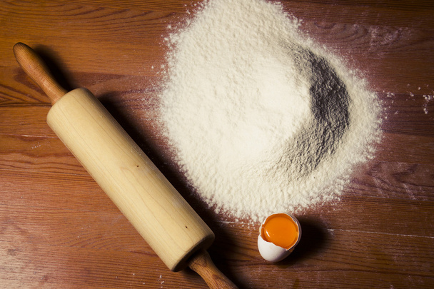 Ingredients for cooking dough on a wooden table. Flour, egg and a rolling pin. - Fotó, kép