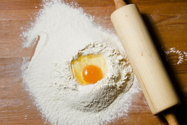 Ingredients for cooking dough on a wooden table. Flour, egg and a rolling pin. - Φωτογραφία, εικόνα