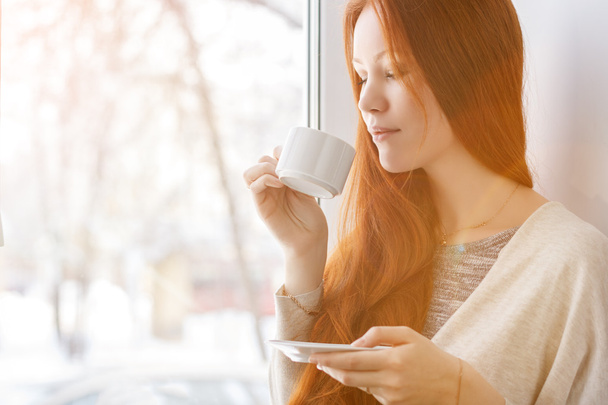 Belle jeune femme avec une tasse de café du matin près de la fenêtre
. - Photo, image