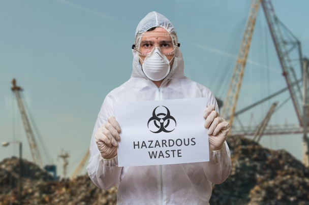 Techniker in Schutzanzug auf Mülldeponie warnt vor gefährlichen Sonderabfällen und Gefahrenmatten. - Foto, Bild