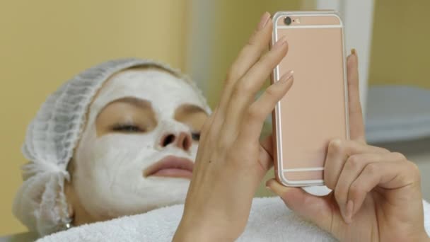 Žena s obličejovou maskou, prohlížení internetu na dotykové obrazovce smartphonu na Spa Salon - Záběry, video