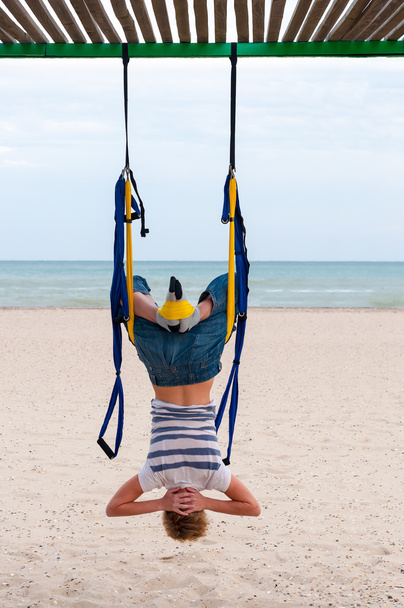 Young woman upside down doing anti-gravity aerial yoga or fly-yoga in hammock on sea background - Foto, afbeelding